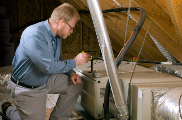A technician examines a furnace in an attic